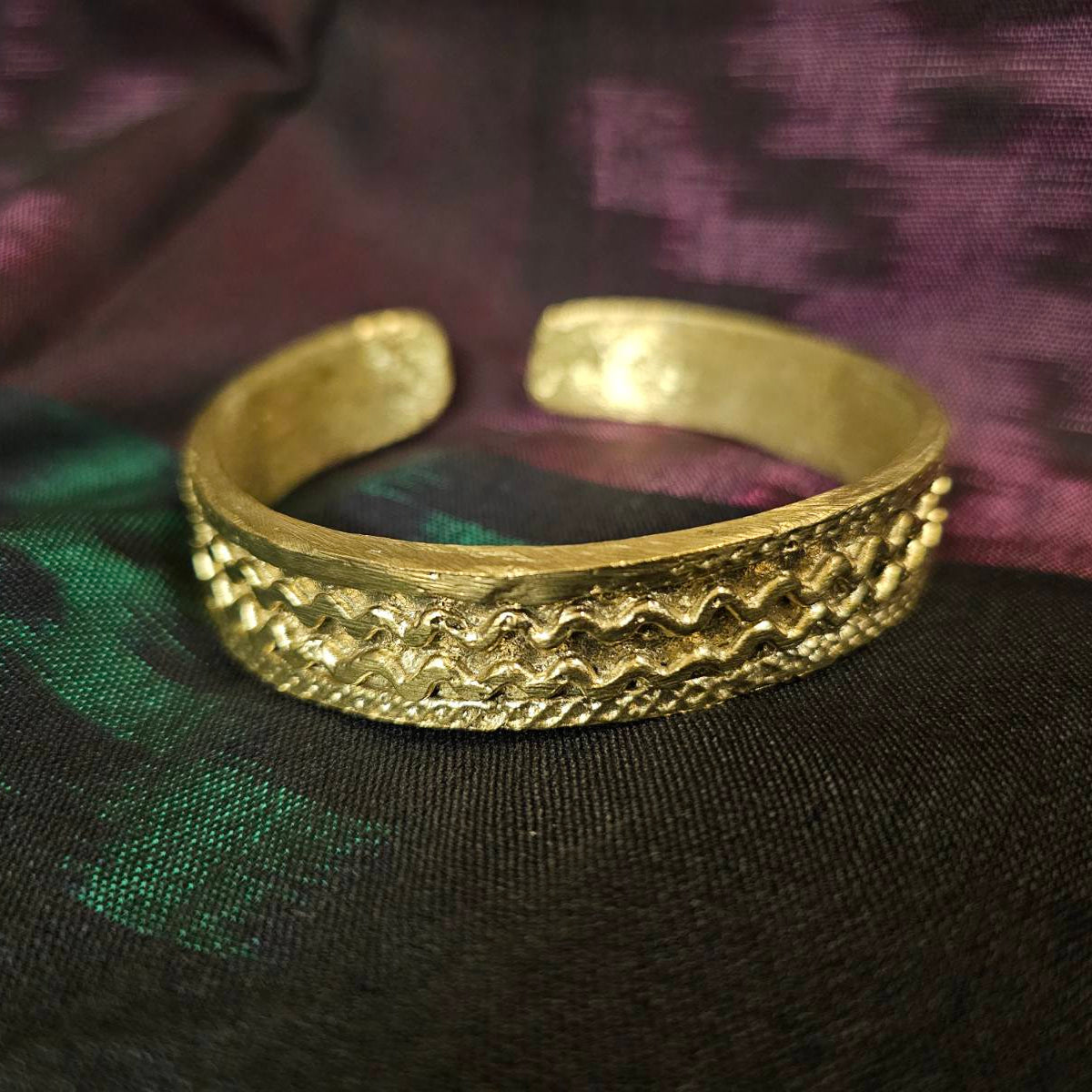 Gold bracelet with intricate design on a dark fabric background